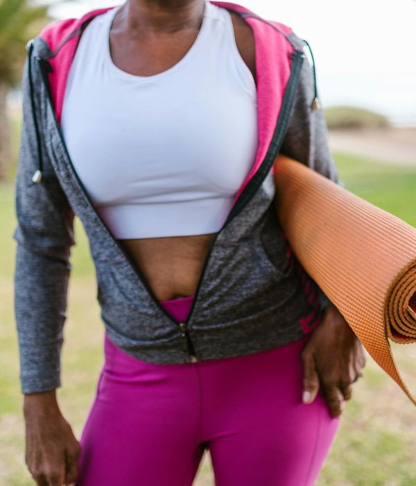 Woman in activewear smiling and stretching in a green park.